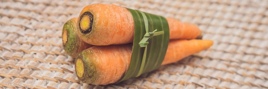 BANNER, LONG FORMAT Eco-friendly product packaging concept. Carrot wrapped in a banana leaf, as an alternative to a plastic bag. Zero waste concept. Alternative packaging.