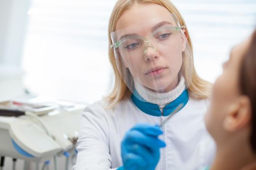 Close up of a professional dentist wearing protective mask, working with her patient. Female dentist examining teeth of her client, working at the dental clinic. Treatment, procedure, medical concept