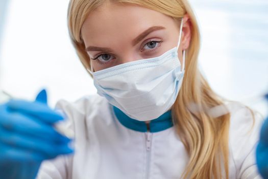 Close up shot of a female doctor reaching out to the camera with medical tools in her hands. Female dentist wearing medical mask ready to examine your teeth. POV shot. Healthcare, dentistry concept