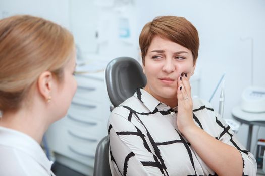 Young woman having toothache, sitting in dental chair at the clinic