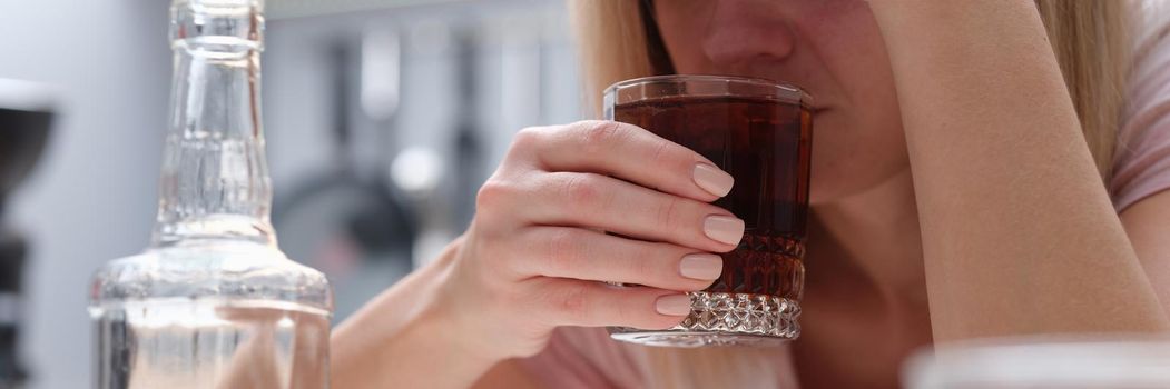 Upset woman drinking alcoholic drink at home in the kitchen, close-up. Female alcoholism, depression. Clouded mind