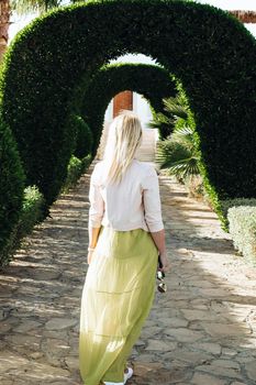 A woman goes forward. View from the back of a walking woman along the alley of arches from green plants