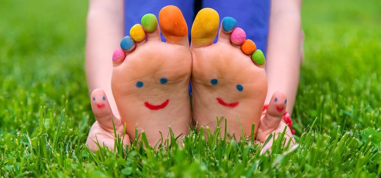 Feet of a child on the grass with a painted smile. Selection focus. Kid.