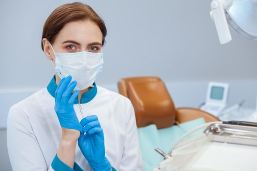 Professional dentist preparing for medical examination, putting on rubber gloves. Female doctor in uniform wearing medical gloves and mask, copy space. Occupation, job, healthcare concept