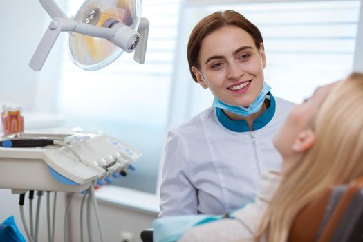 Cheerful female dentist smiling joyfully, talking to her patient during dental examination, copy space. Friendly dentist consulting her client, working a dental clinic. Healthcare concept