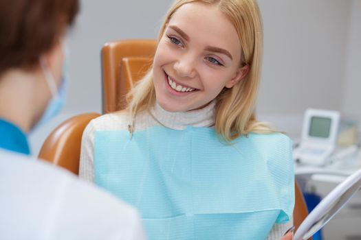 Young cheerful blond haired woman smiling joyfully during medical consultation with her dentist. Lovely female patient visiting dentist. Professional medical care, health, treatment concept