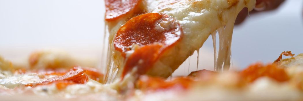 The hand takes a large slice of hot pizza with sausage, close-up. Traditional portion of Italian fast food, melted cheese