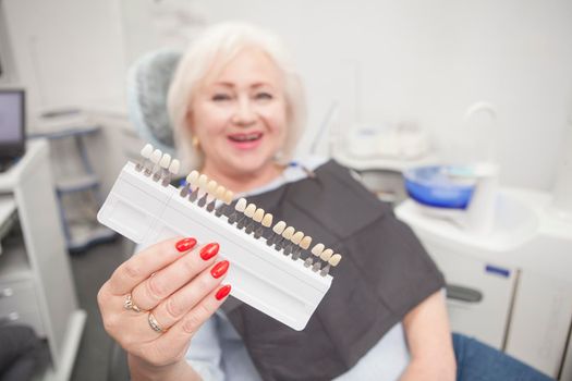 Senior woman laughing, hoding out teeth whitening shade chart to the camera at dental clinic