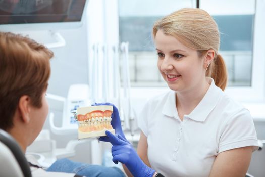 Young female dentist talking to her patient, working at her clinic