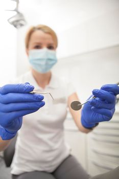 Vertical shot of a professional dentist reaching out to the camera with her dental tools