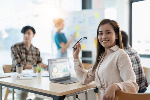 Group of young asian business people in smart casual wear working together in creative office using laptop