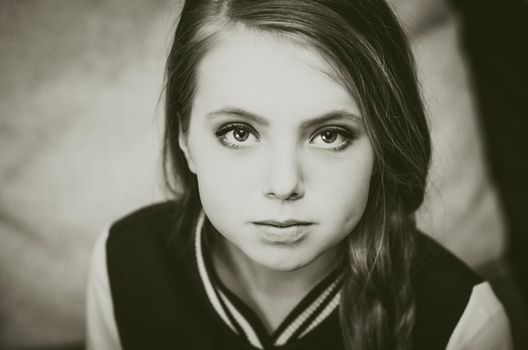 Black and white photo of a young teenage girl looking directly at the camera. Evening makeup for stage performances. dimple on the cheek, hair in a plait, large painted eyes, plump lips, straight nose