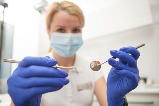 Professional dentist holding out dental instruments to the camera