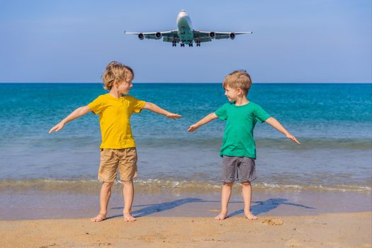 Two happy boys have fun on the beach watching the landing planes. Traveling on an airplane with kids concept. Text space. Island Phuket in Thailand. Impressive paradise. Hot beach Mai Khao. Amazing landscape.