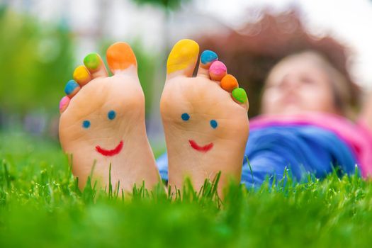 Feet of a child on the grass with a painted smile. Selection focus. Kid.