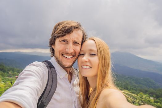 Man and woman making selfie on background of Batur volcano and Agung mountain view at morning from Kintamani, Bali, Indonesia.