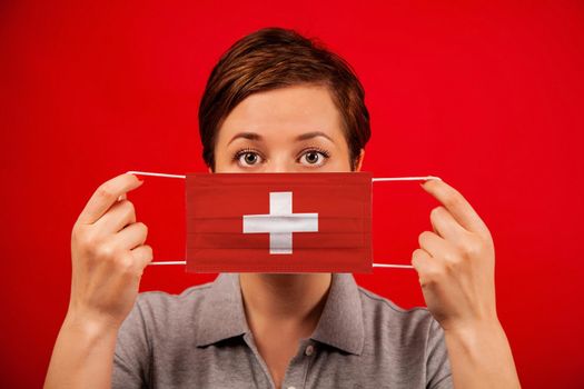 Coronavirus COVID-19 in Switzerland. Woman in medical protective mask with the image of the flag of Switzerland. The concept of preventing the spread of the epidemic and treating coronavirus.
