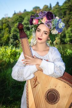 Young Ukrainian woman in a national white shirt hugs a bandura.