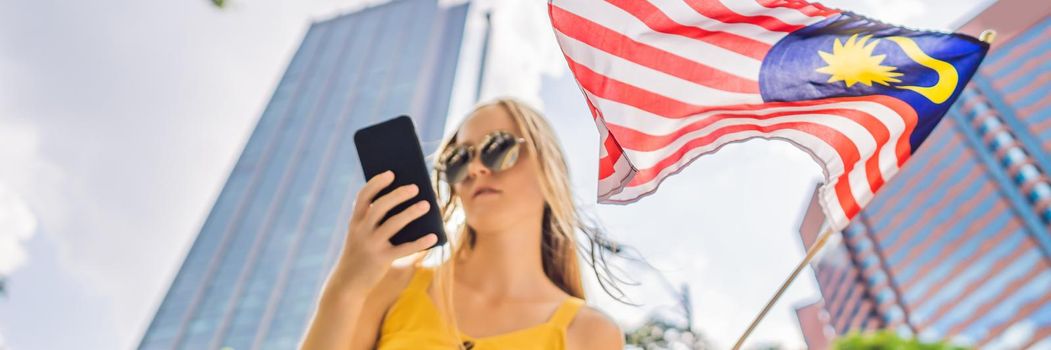 Travel and technology. Young woman tourist with the flag of Malaysia is looking at a city map in a smartphone for navigation. BANNER, LONG FORMAT