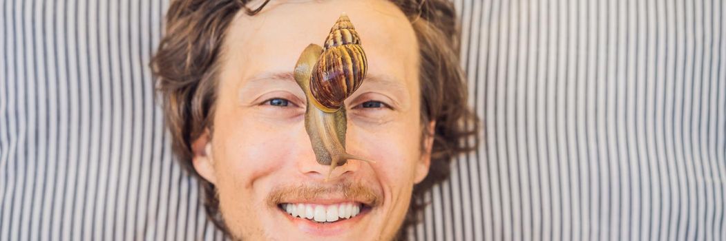 Young man makes a face mask with snail mucus. Snail crawling on a face mask. SPA for man, SPA for all. BANNER, LONG FORMAT