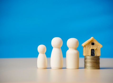 Three wooden figures people standing nearby of tiny wooden house on stack coins. Concept for family, loan, property ladder, financial, mortgage, real estate investment, taxes and bonus.