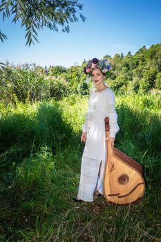 Beautiful Ukrainian woman in a white national dress stands with a bandura on a summer sunny day.