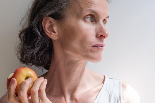 Profile of middle aged woman with grey hair holding red apple (selective focus)
