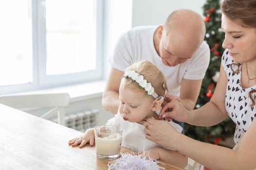 Mother and father helps to put on cochlear implant for their deaf baby daughter in christmas living room. Hearing aid and innovating medical technologies treatment deafness