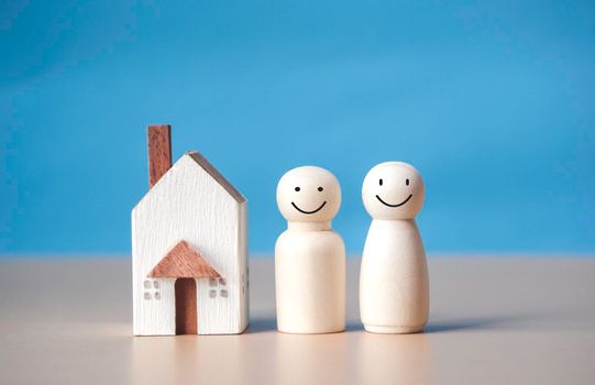 Two wooden figures of people with happiness and a house on blue background. Affordable housing and mortgages for buying concept young family and couples. family nest and copy space.