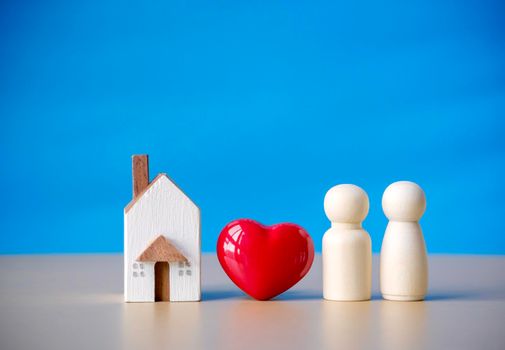 Family wooden figure standing near red heart and miniature house symbol. Concept of love of relationship family, couple life and happiness with blue background.