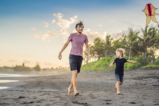 Young father and his son running with kite on the beach.