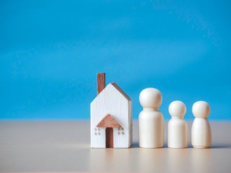 Four wooden figures people standing nearby of tiny wooden house. Concept for family, loan, property ladder, financial, mortgage, real estate investment, taxes and bonus.
