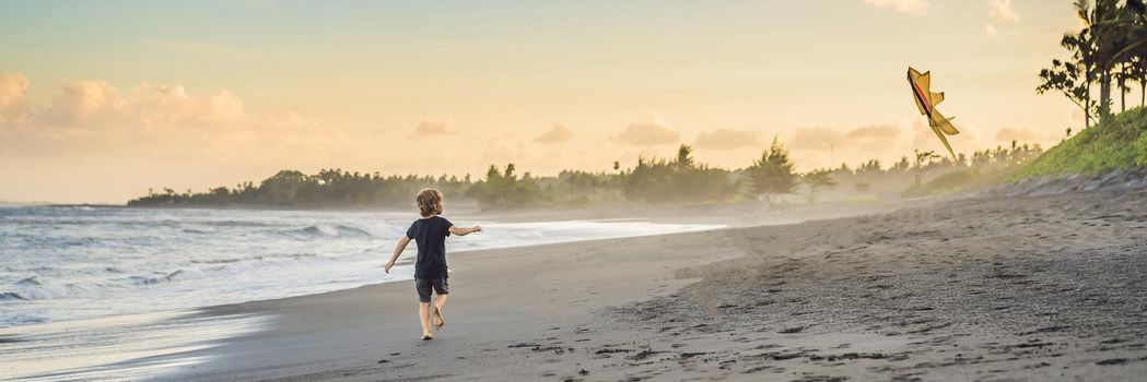 Happy young boy flying kite on the beach at sunset. BANNER, LONG FORMAT