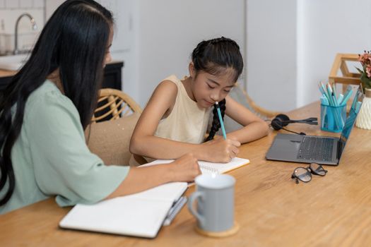 Mother and asian kid little girl learning and looking at laptop computer making homework studying knowledge with online education e-learning system. children video conference with teacher tutor at home.