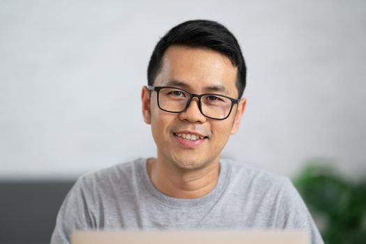 freelance man in eyewear smiling and working with laptop remotely, sitting at wooden table. Pleasant happy man communicating in social network, searching information online.