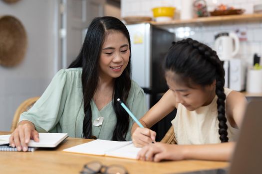 Mother and asian kid little girl online learning on laptop computer making homework studying knowledge with online education e-learning system. children video conference with teacher tutor at home.