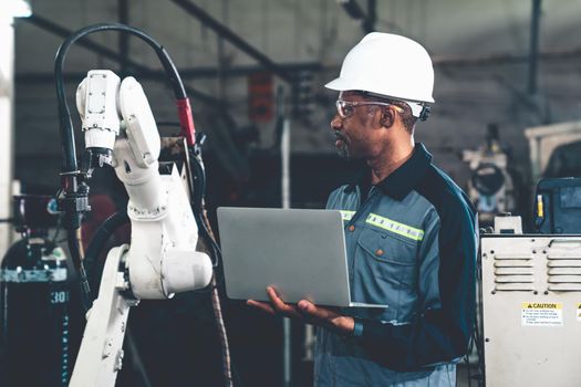 African American factory worker working with adept robotic arm in a workshop . Industry robot programming software for automated manufacturing technology .