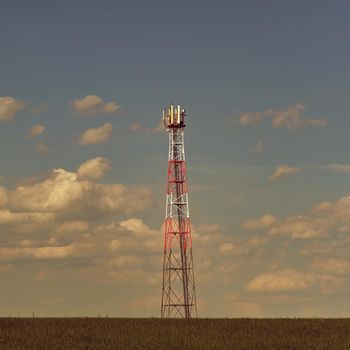 Transmitter for gsm signal of mobile phones in the field. In the background blue sky with clouds. Concept for modern technology and industry - Telecommunication Tower.