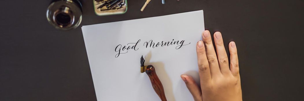 BANNER, LONG FORMAT Good morning. Calligrapher Young Woman writes phrase on white paper. Inscribing ornamental decorated letters. Calligraphy, graphic design, lettering, handwriting, creation concept.