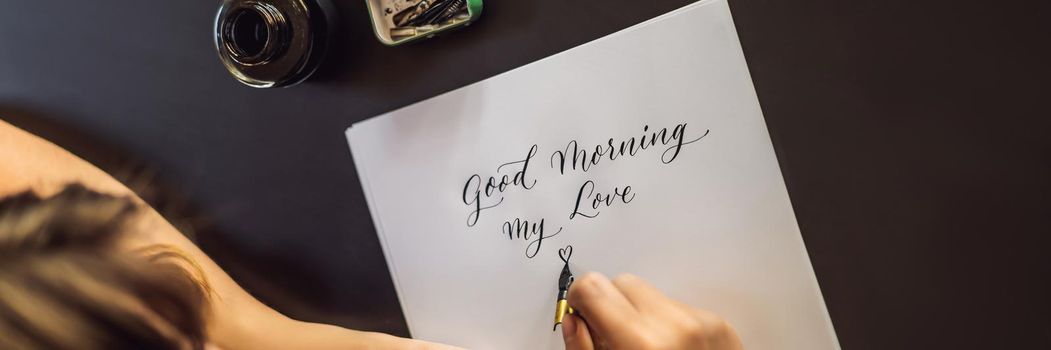 BANNER, LONG FORMAT Good morning. Calligrapher Young Woman writes phrase on white paper. Inscribing ornamental decorated letters. Calligraphy, graphic design, lettering, handwriting, creation concept.