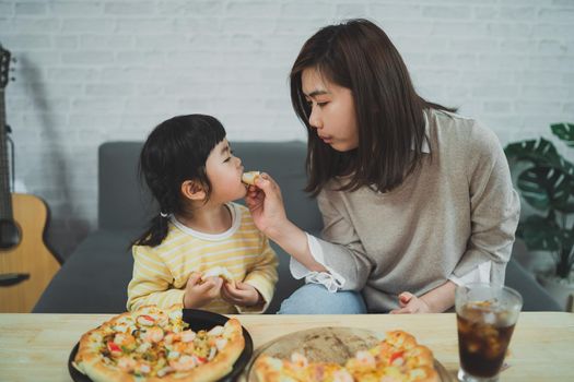 Asian mothers and children do activities at home. Mother is going to feed pizza for her kids. Children are eating and tasting italian homemade pizza.