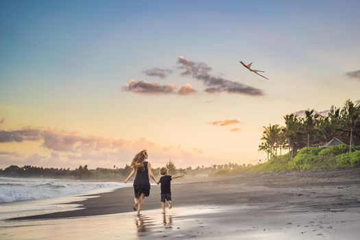 Mom and son are running on the sea beach launching a kite.