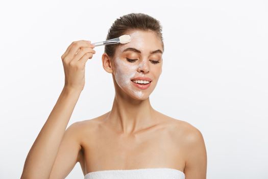 Portrait beautiful naked woman apply cosmetic white clay mask on with brush. Isolated on a white background. concept of beauty and health.