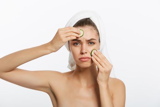 Woman with facial mask and cucumber slices in her hands on white background.