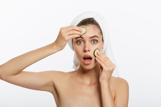 Woman with facial mask and cucumber slices in her hands on white background.