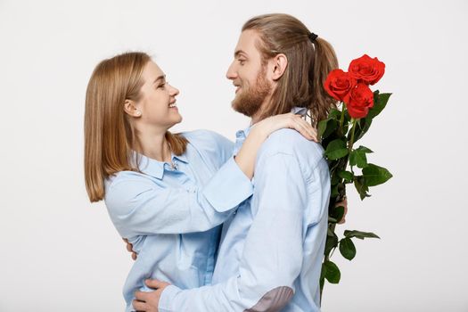 Portrait of an attractive young man hiding flowers from his girlfriend before giving her a surprise over white isolated background .