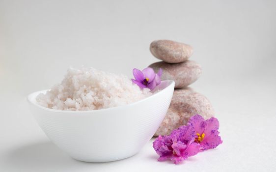 White bowl with pink salt, flowers and stones on a white background