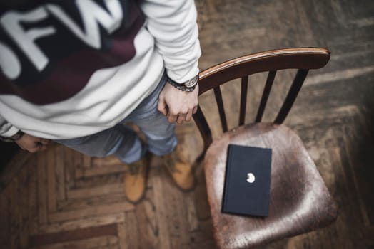 The black book lies on a brown wooden chair. The guy at the library holds a hand on a chair. The room is in a wooden style. wooden file cabinet racks