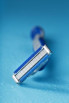 Shaving machine with three blades on a blue background with water drops in close-up. The concept of purity and freshness