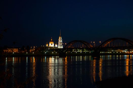 Nocturnal image of the passage of a river through the city where there is a bridge, houses, streetlights and at the end the belfry of the city cathedral.